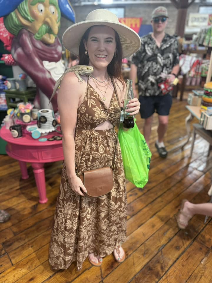 woman in brown dress and tan hat with bearded dragon on her shoulder